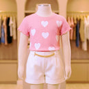 Manequim infantil vestindo conjunto elegante: blusa rosa de corações e short branco de alfaiataria.
