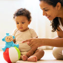 Close de um bebê interagindo com brinquedo sensorial em formato de macaco azul sobre uma bola.