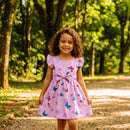 menina usando no jardim vestido de borboleta na cor lilás com estampa de borboleta