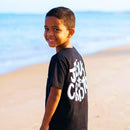 Menino olhando para o mar usando camiseta cristã preta e bermuda jeans.